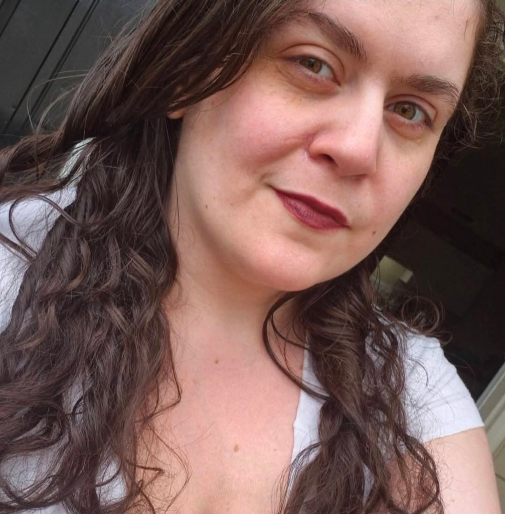 Mandee with long, dark wavy hair and burgundy lipstick, smiling at the camera.